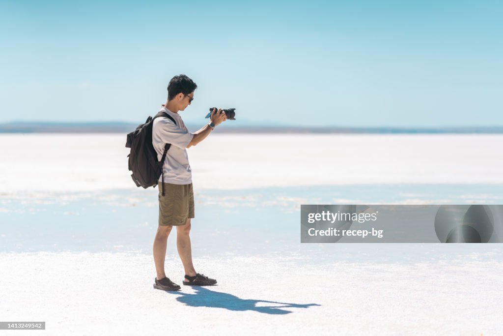 Young male tourist taking videos and photos with his camera on white salt in Salt Lake