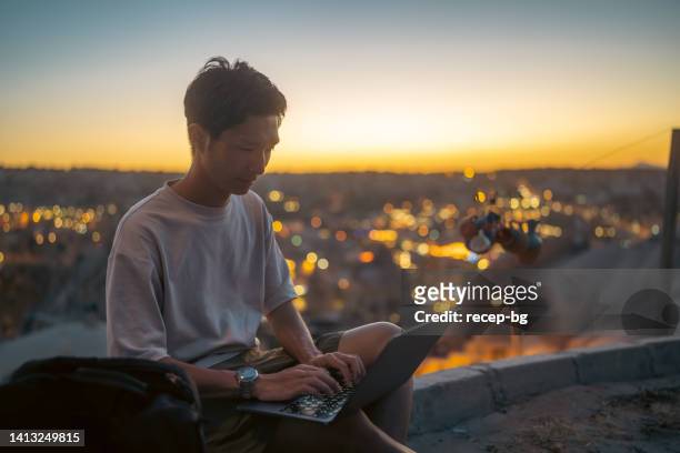 young male freelance photographer videographer tourist using laptop on hill during sunset during his vacation - wonderlust computer stock pictures, royalty-free photos & images