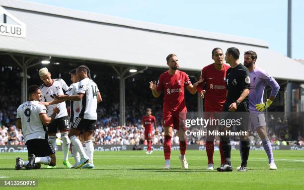 Players of Fulham help Aleksandar Mitrovic to their feet as Jordan Henderson and Virgil van Dijk of Liverpool protest to Referee Andy Madley during...