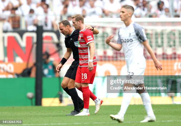 Referee Bastian Dankert is helped off the pitch by Andre Hahn of Augsburg during the Bundesliga match between FC Augsburg and Sport-Club Freiburg at...