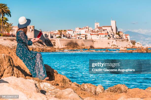 tourist reading a book with scenic antibes in the background, cote d'azur, france - antibes stock pictures, royalty-free photos & images