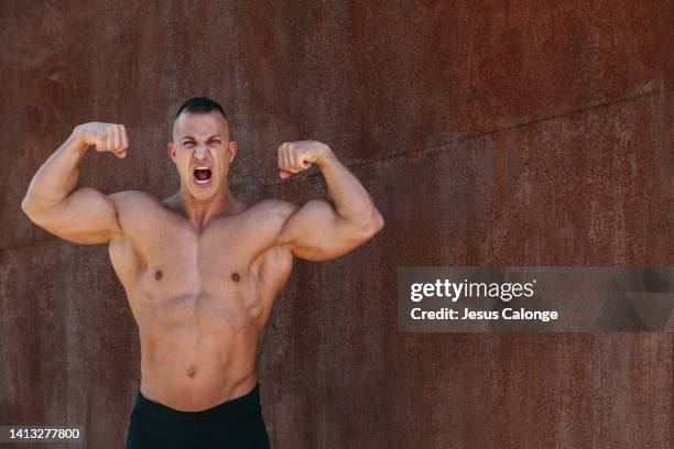 male bodybuilder with his arms in the air, shouting. with an expression of effort and anger. men, bodybuilding, sport concept - masculinidade imagens e fotografias de stock