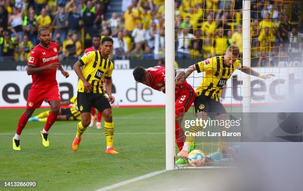 Marco Reus of Borussia Dortmund scores their side's first goal whilst under pressure from Piero Hincapie of Bayer Leverkusen, after a shot by Karim...
