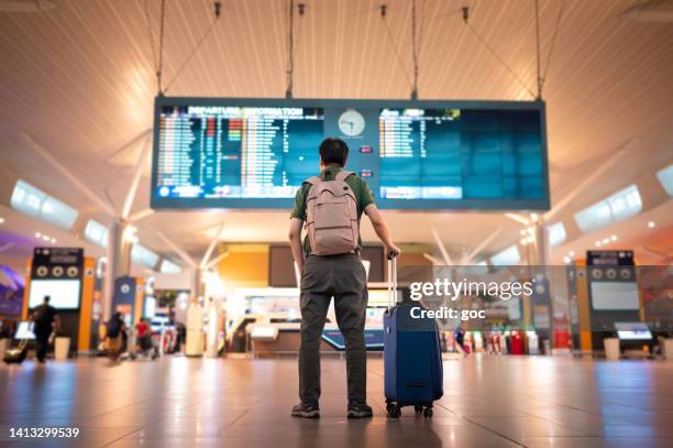 turista masculino mirando el tablero de llegada y salida en el aeropuerto internacional de kuala lumpur - travel fotografías e imágenes de stock