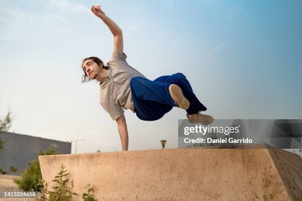 boy with ponytail jumping in a public park, jumps, stunts and free running, dancing - freestyle dance stock pictures, royalty-free photos & images