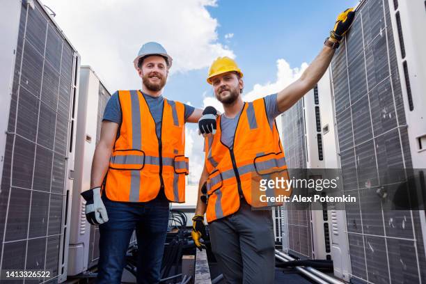 屋根のエアコンの近くでポーズをとるエンジニアと技術者。 - alex pix ストックフォトと画像