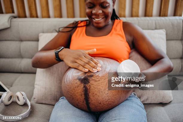 pregnant woman applying cream on her stomach - belly rub stockfoto's en -beelden