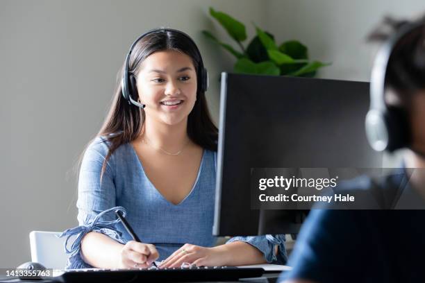 junge frau, die im callcenter arbeitet, nimmt anrufe über das headset entgegen, während sie auf den computerbildschirm schaut - filipino ethnicity and female not male stock-fotos und bilder