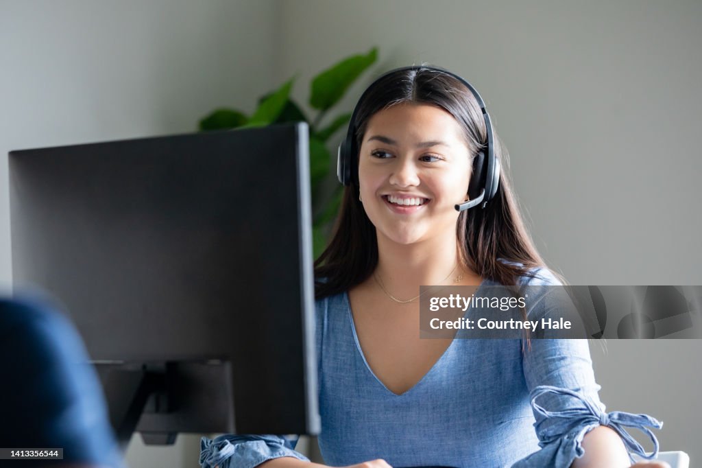 Junge Frau, die im Callcenter arbeitet, nimmt Anrufe über das Headset entgegen, während sie auf den Computerbildschirm schaut