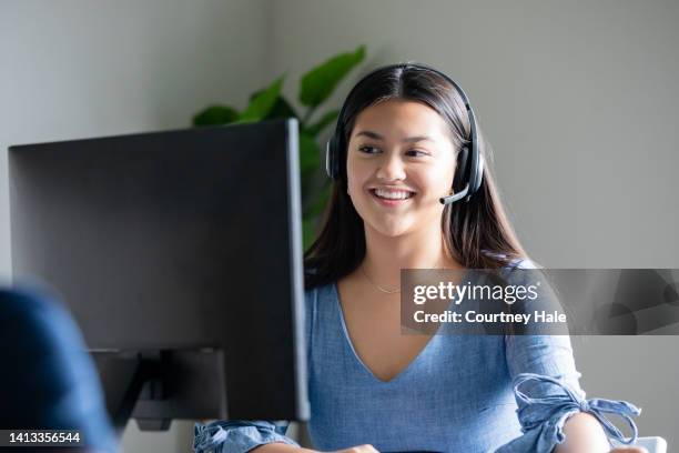 junge frau, die im callcenter arbeitet, nimmt anrufe über das headset entgegen, während sie auf den computerbildschirm schaut - philippinischer-abstammung stock-fotos und bilder