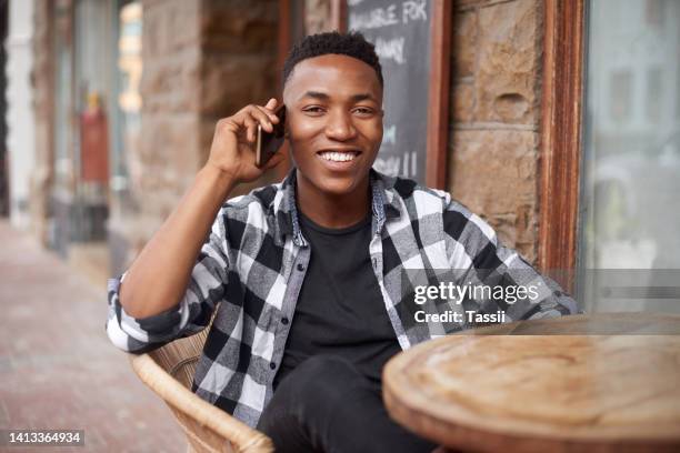 homem negro feliz, moderno e despreocupado em um telefonema enquanto relaxava na cidade, aproveitando seu tempo livre no fim de semana. homem afro-americano sorrindo enquanto fala e espera em um café ao ar livre - café da internet - fotografias e filmes do acervo