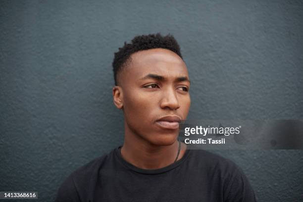 edgy, trendy and serious young man posing against a dark wall with copy space. face and head of a young, stylish and fashionable african american male looking away and thinking on a grey background - male model casual imagens e fotografias de stock