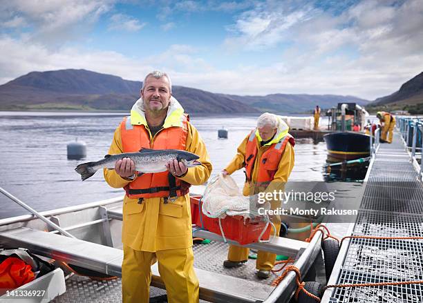 portrait of fisherman with freshly caught salmon on loch of scottish salmon farm - aquacultuur stockfoto's en -beelden