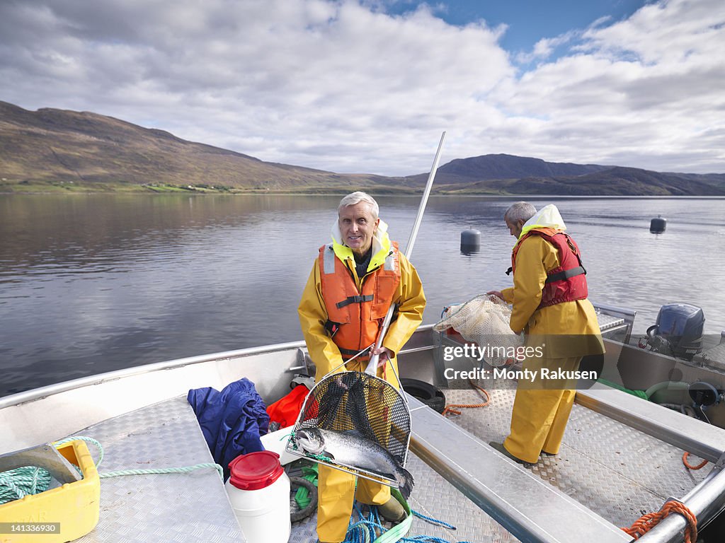 Portrait of fisherman with freshly caught salmon in net on loch of Scottish salmon farm
