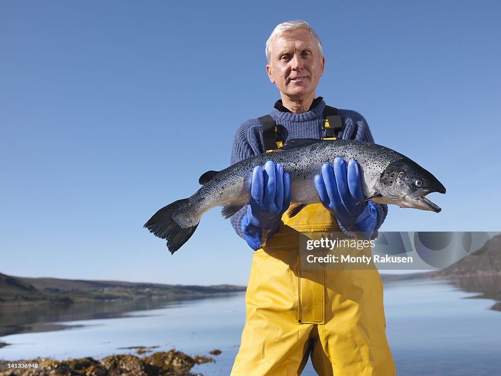 Portrait of fisherman standing in loch holding freshly caught salmon