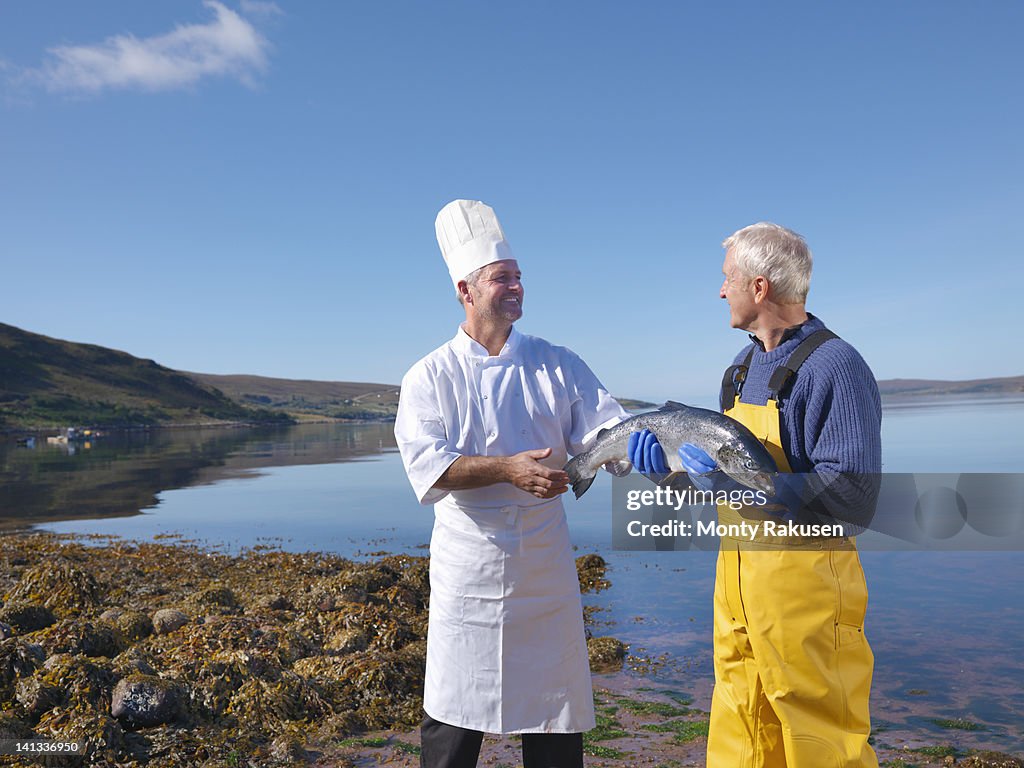 Fisherman in loch giving freshly caught salmon to chef