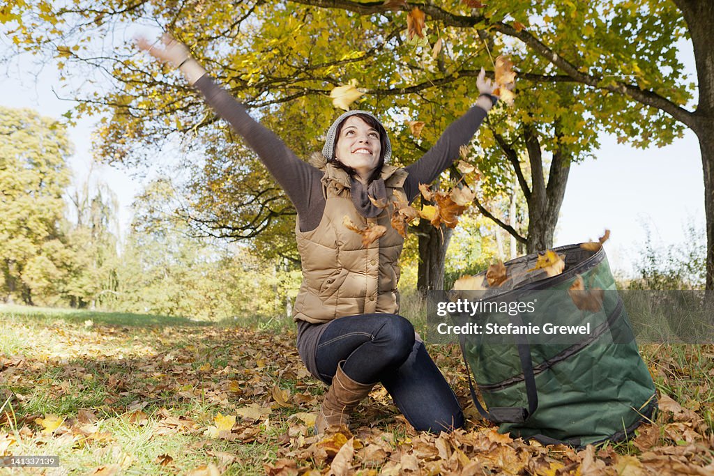 Woman playing with fall leaves in park