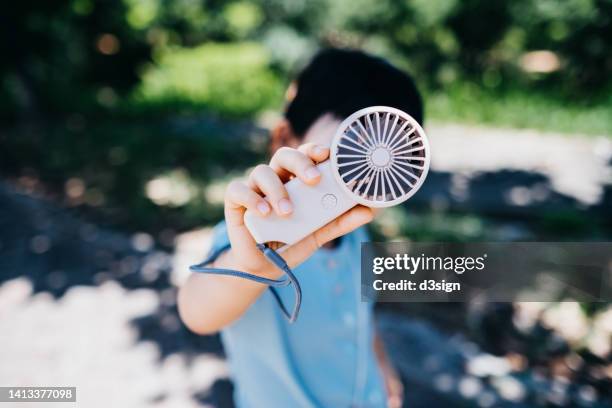 portrait of lovely little asian girl holding a handheld electronic fan to cool herself down in hot summer day outdoors - electric fan stock pictures, royalty-free photos & images