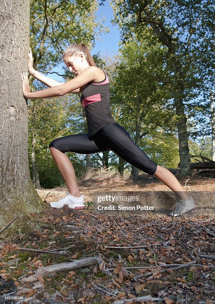 Runner stretching against tree in park