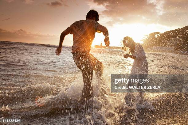 couple playing in waves at beach - männer ausflug fun stock-fotos und bilder