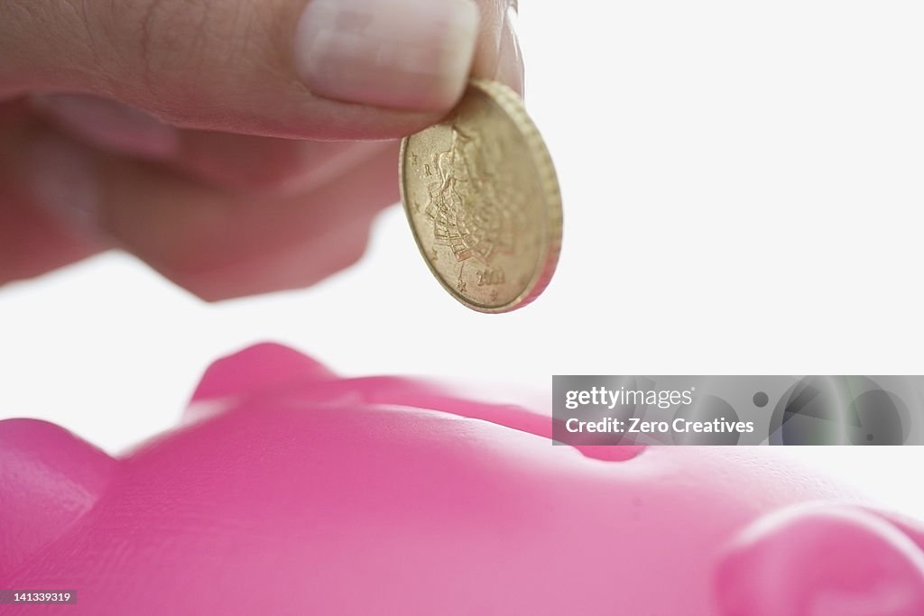 Close up of woman feeding piggy bank