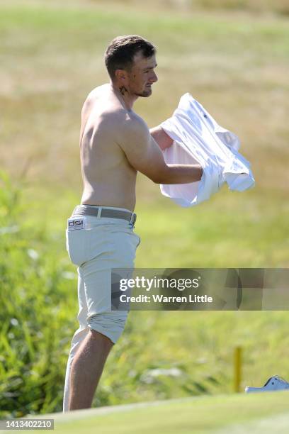 Paul Dunne of Ireland puts their shirt back on after playing their second shot out of the pond on the 3rd hole during day four of the Cazoo Open at...