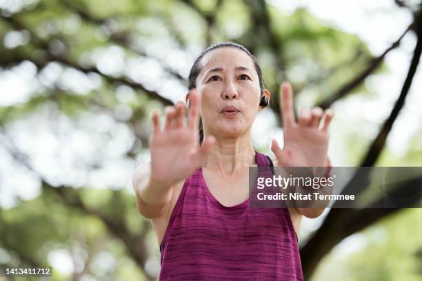 tai chi and mind-body breathing can make you better, faster, and stronger. middle-aged asian woman taking tai chi at a public park. she is practicing tai chi or qi gong poses and set her breath inhaling and exhaling. - tai chi stock pictures, royalty-free photos & images
