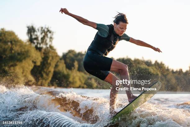 young beautiful woman training wake surfing elements behind the boat against summer greenery background - adrenalin stock-fotos und bilder