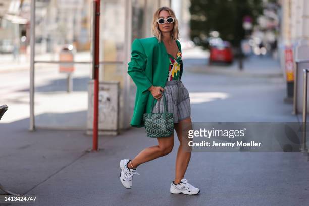 Karin Teigl wearing Holzweiler puffed grey shorts, Thierry Mugler colorful corset, New Balance white navy blue sneaker, Goyard logo print green mini...