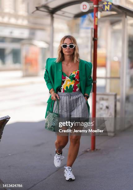 Karin Teigl wearing Holzweiler puffed grey shorts, Thierry Mugler colorful corset, New Balance white navy blue sneaker, Goyard logo print green mini...