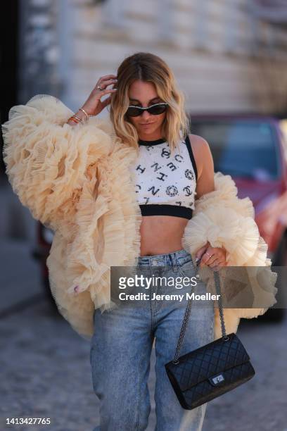 Karin Teigl wearing Chanel 2.55 black leather bag, Chanel black logo shades, Chanel logo black and white bra cropped top, Cambio wide leg jeans and...
