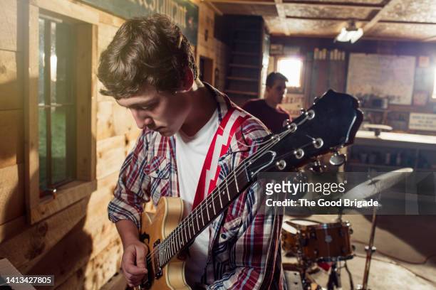 teenage boy looking down while playing guitar in garage - plaid shirt stock pictures, royalty-free photos & images