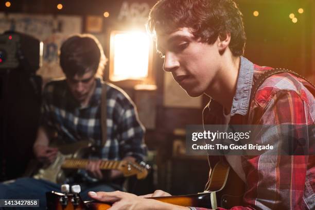 teenage boy playing guitar with friend while doing rehearsal in garage - saiteninstrument spielen stock-fotos und bilder