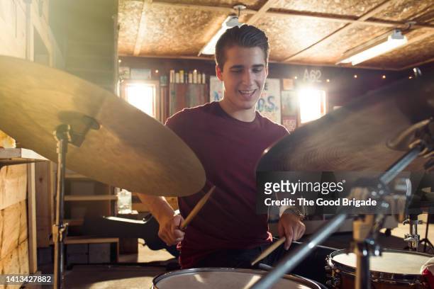 smiling teenage boy practicing on drums in garage - drummer stock pictures, royalty-free photos & images