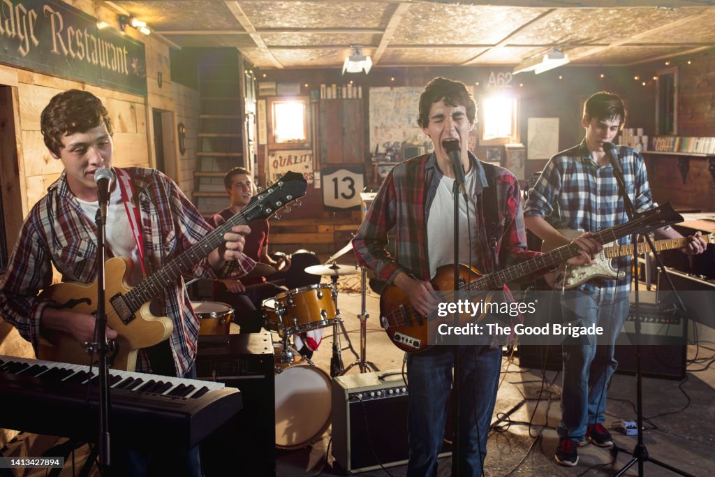Teenage friends singing and playing guitar during band practice in garage