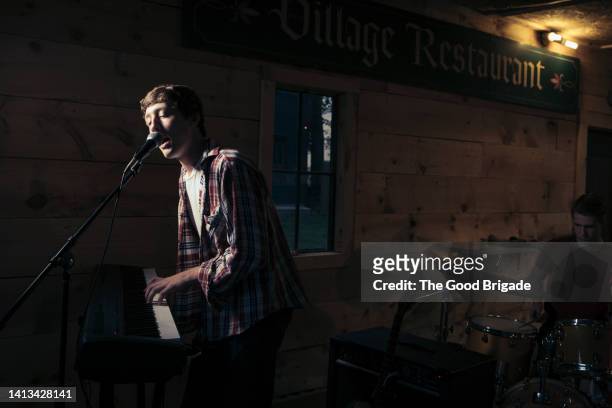 teenage boy singing while playing piano with friend practicing drums in background - boy band stockfoto's en -beelden