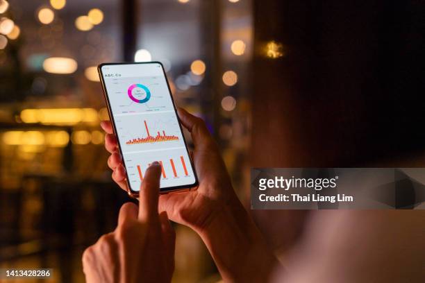 woman checking and analysing stock market data with mobile app on smartphone - portfólio imagens e fotografias de stock
