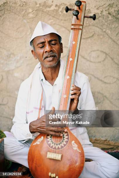 a senior man from rural india playing the tambora, a musical instrument - sitar stockfoto's en -beelden