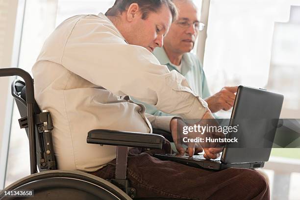 quadriplegic man with spinal cord injury in wheelchair using his thumb to type on computer - quadriplegic stock-fotos und bilder