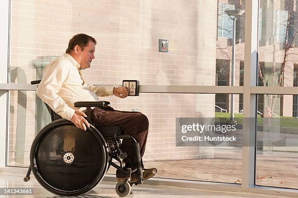 businessman with spinal cord injury in wheelchair using automatic door opener at office building entrance - quadriplegic stock-fotos und bilder