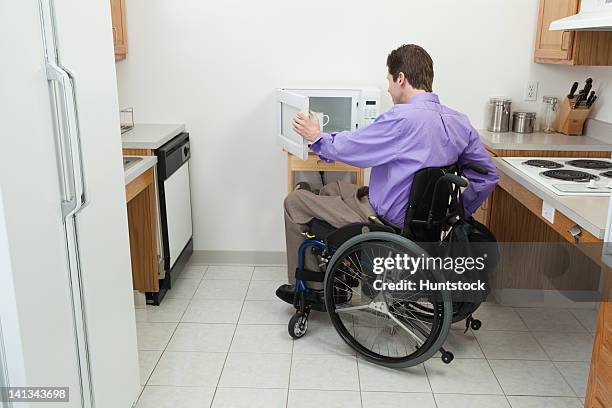 man in wheelchair with spinal cord injury opening accessible microwave - rolstoelvriendelijk stockfoto's en -beelden