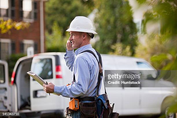 telecommunications installer using work order at his truck and talking on a cell phone - repairman phone stock pictures, royalty-free photos & images