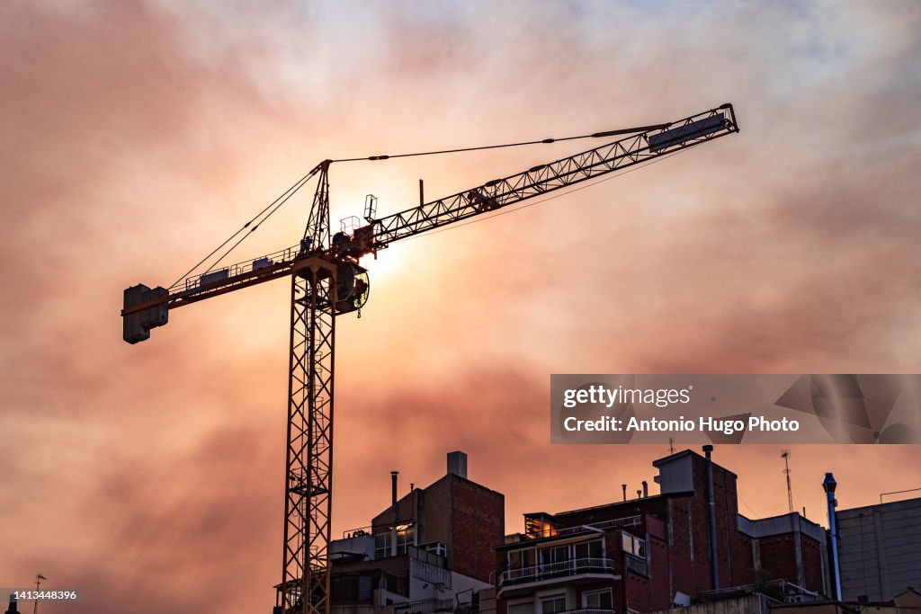 Crane over some buildings. Reddish sky at sunset.