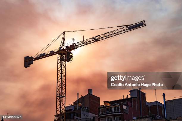 crane over some buildings. reddish sky at sunset. - construcción fotografías e imágenes de stock