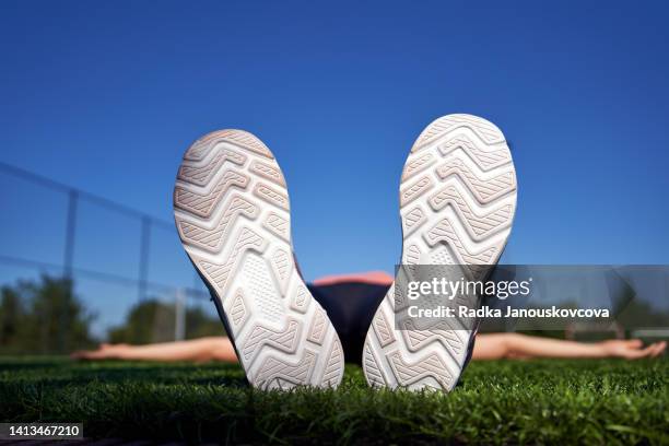 running shoe soles of a tired runner lying on artificial grass at a sports playground - schoenzool stockfoto's en -beelden