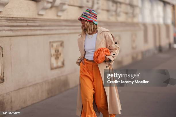 Karin Teigl wearing COS orange wide leg pants, Weat knit colorful bucket hat, beige oversized statement trenchcoat and CYK by constantly k white...