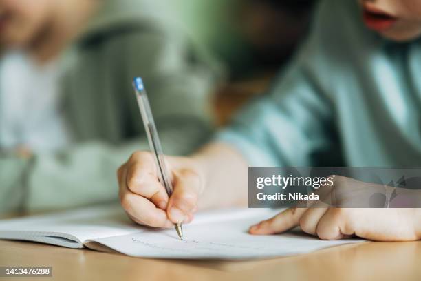 primer plano de un niño escribiendo con un bolígrafo en un libro de trabajo - ensayo fotografías e imágenes de stock