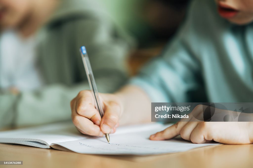 Close-up of a boy writing with a pen in workbook