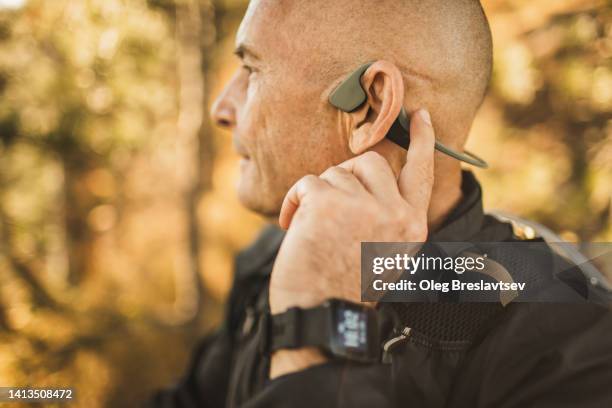 senior man wearing bone conduction headphones to listen music on forest walk or hike. close up - in ear headphones stock-fotos und bilder