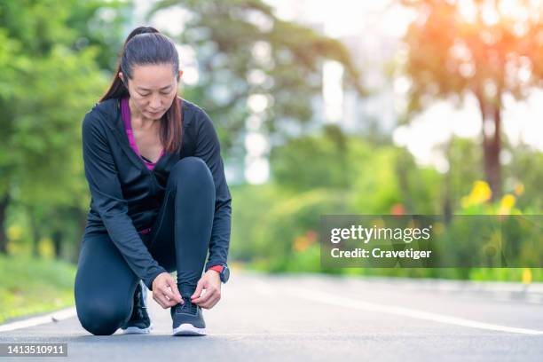 low angle view of a female runner kneeling down to tie shoelaces on a sports track for ankle support and reduce injuries during workout exercise in a public park in the urban environment.shallow depth of field - knoten lösen stock-fotos und bilder